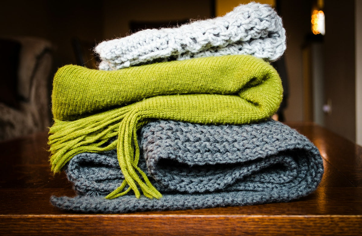 Three folded wool blankets in grey, green and white