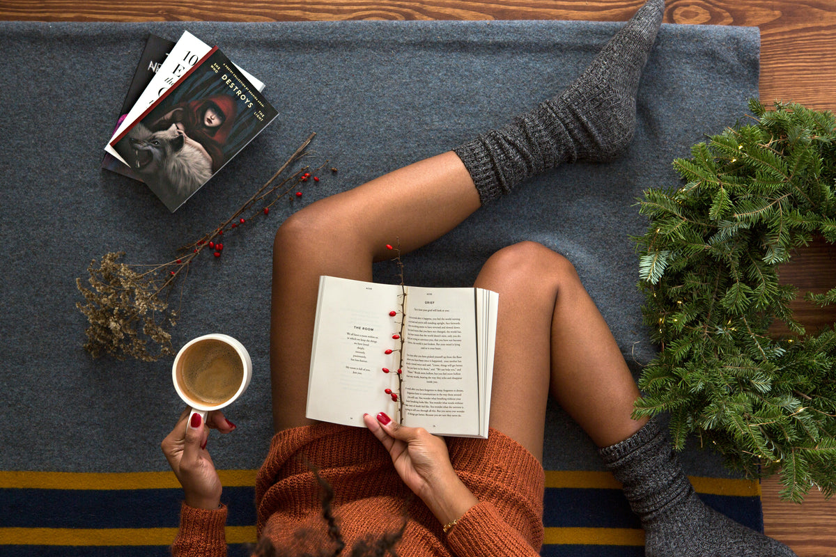 An open book resting on a lap beside a pair of grey wool socks