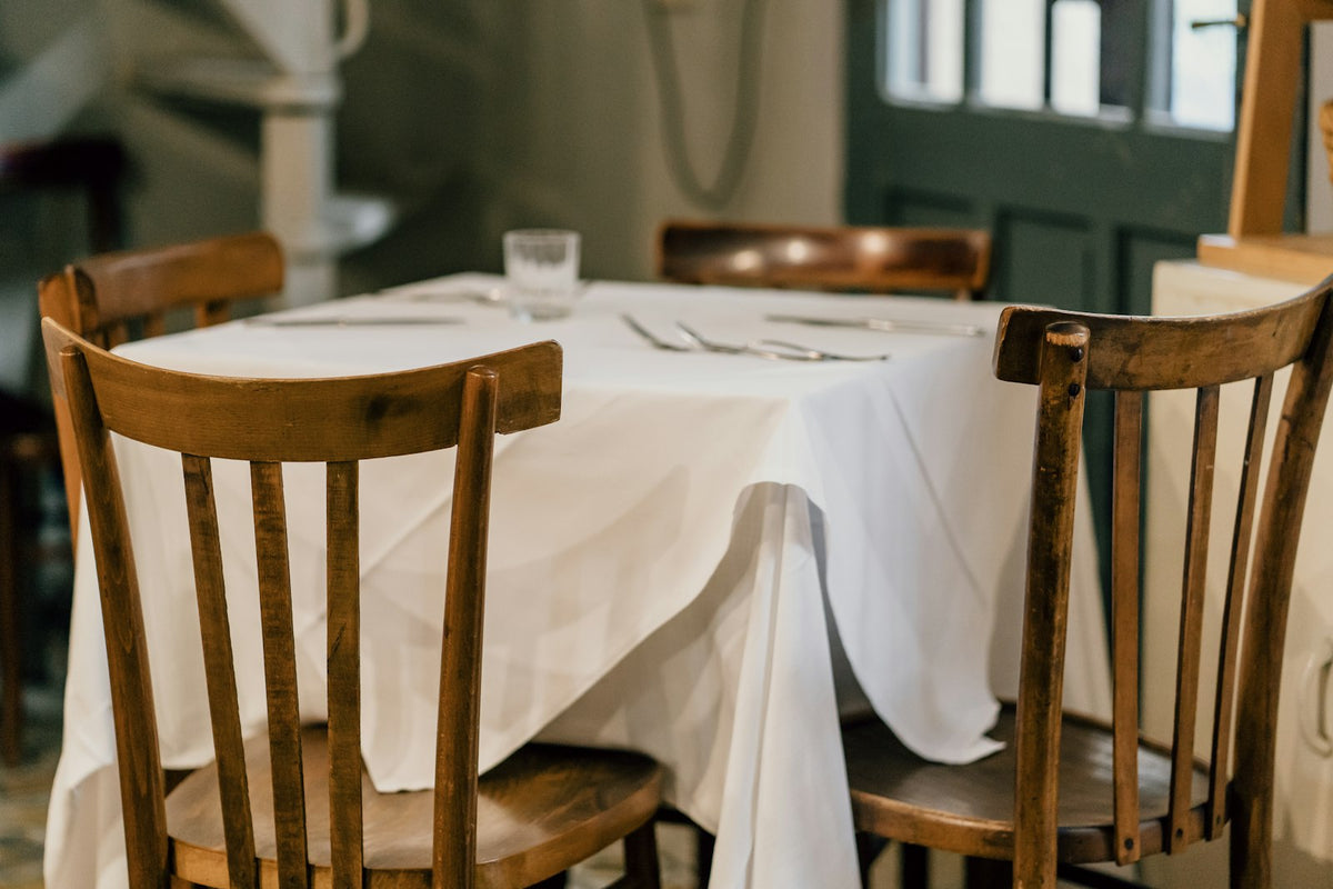 An old-fashioned dining table laid with a cloth and wooden chairs