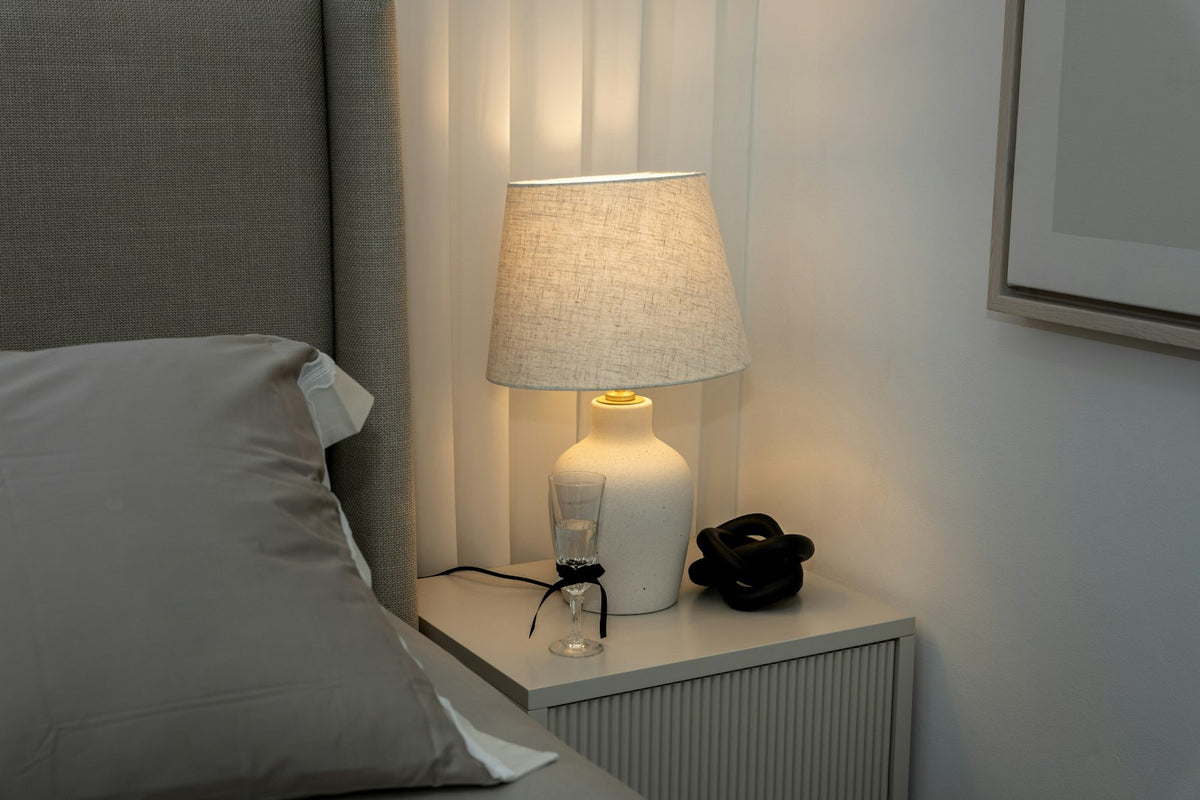 A table lamp with a fabric shade on a bedside table